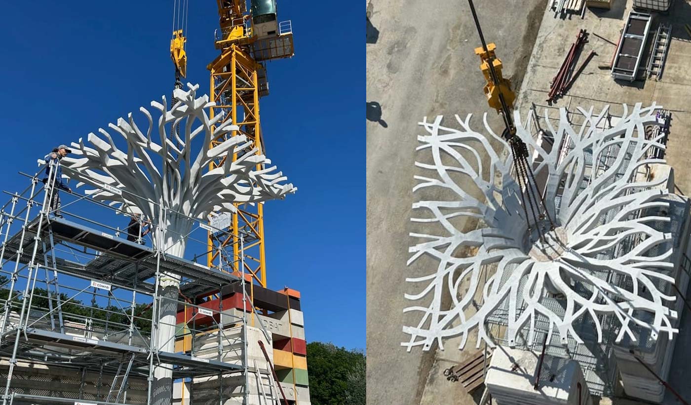 Une grande structure en acier blanc avec des bras ramifiés est montée sur un échafaudage à l'aide d'une grue.