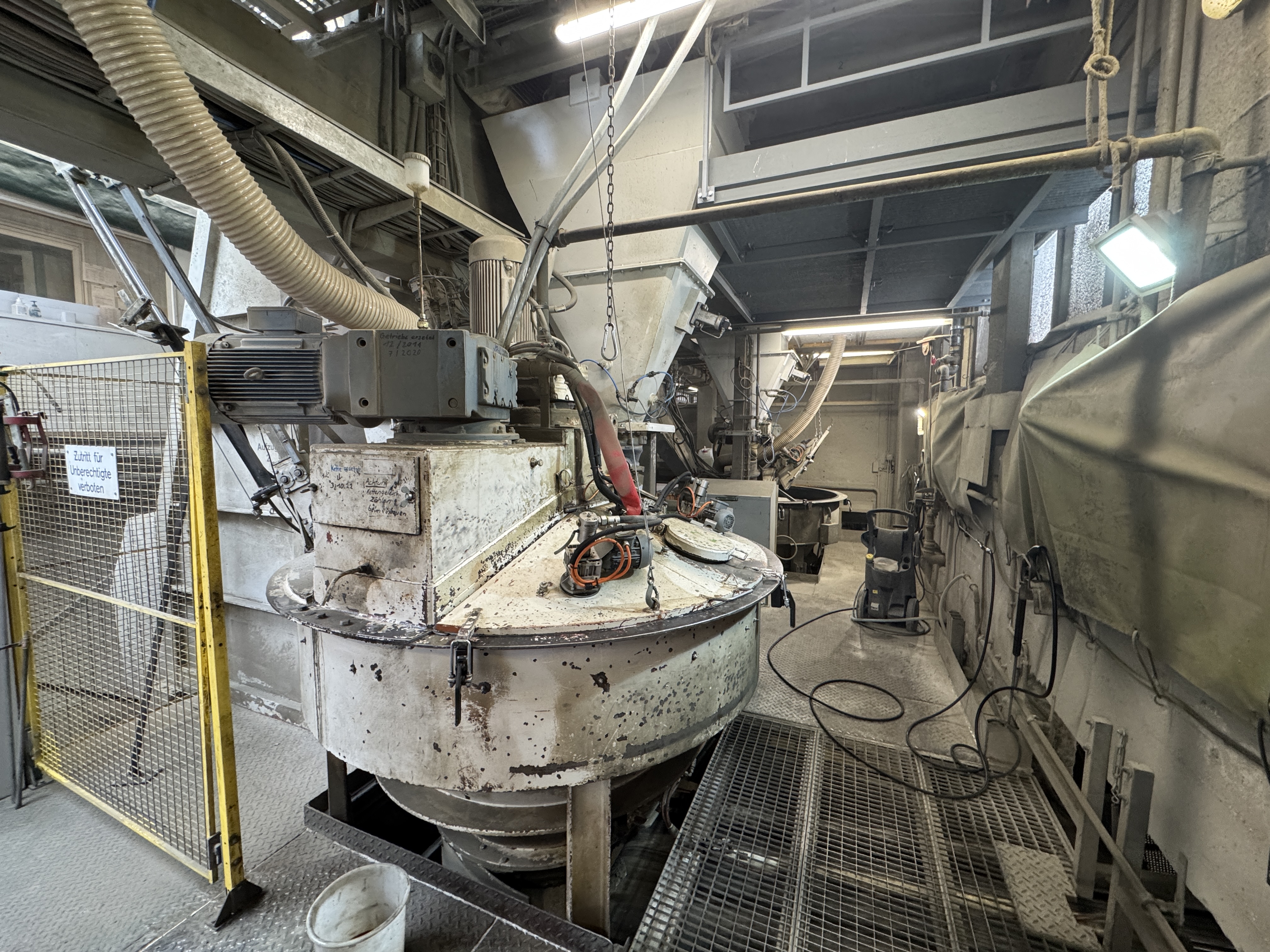 Large, white Kniele KKM mixer with motor, with a mesh floor beneath it in a cramped workshop.
