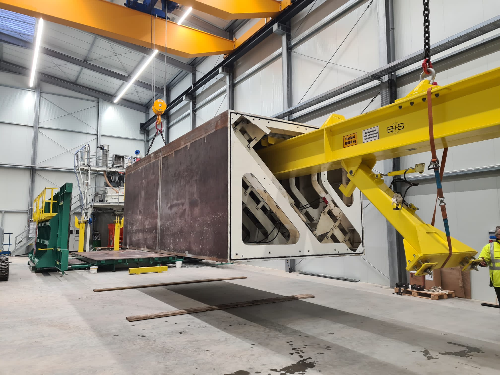 Großes Betonfertigteil wird mit einem Hebegerät in einer Produktionshalle transportiert.