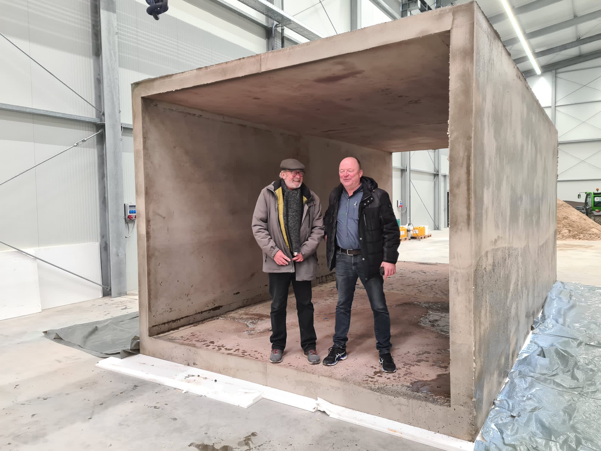 Zwei Personen stehen in einem großen Betonfertigteil in einer Industriehalle.