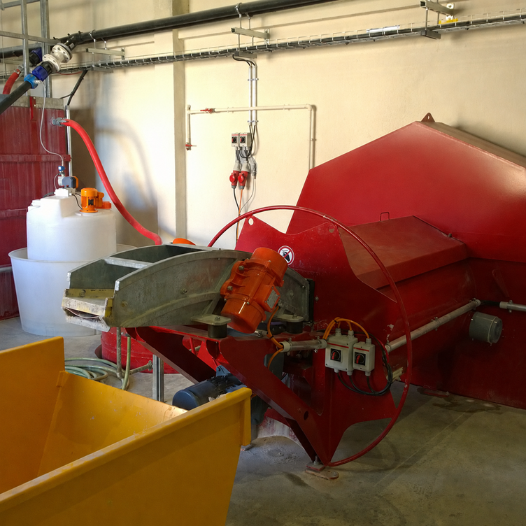 A red washout unit at a recycling plant, complete with feed system, pipework and collection tank, in a production environment.